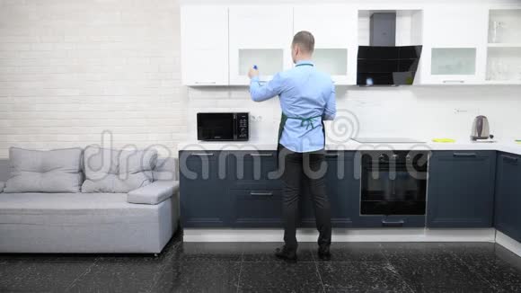 穿着围裙和领带的帅哥打扫公寓里的厨房视频的预览图
