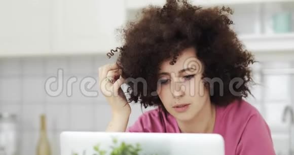 年轻女性自由职业者的肖像卷发在厨房的笔记本电脑上工作视频的预览图