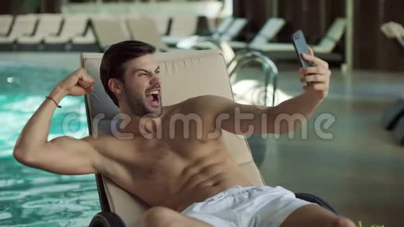 贴身男在室内游泳池附近玩男人在手机上自拍视频的预览图
