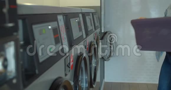 女人正在把五颜六色的衣服放进洗衣机里同时衣服在烘干机里烘干和旋转视频的预览图