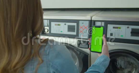 女士在洗衣店洗衣服时使用带有绿色屏幕的智能手机铬钥匙快关门视频的预览图
