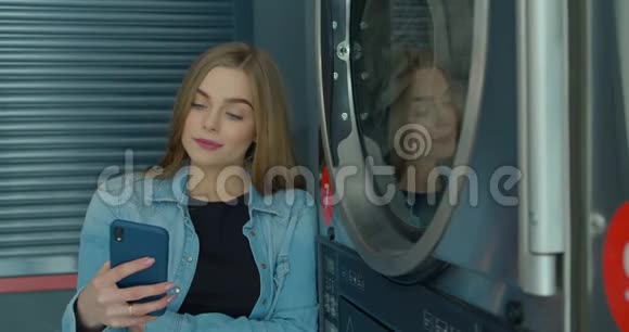 女人在洗衣店洗衣服时使用智能手机视频的预览图