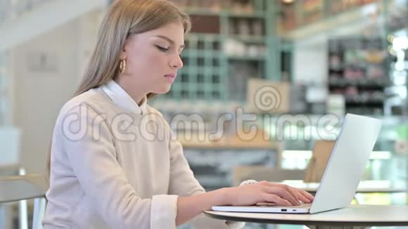 带着脖子疼的年轻女人在咖啡馆里用笔记本电脑视频的预览图