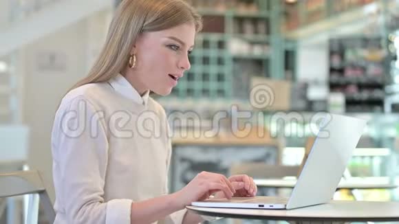 年轻女子在咖啡馆里用笔记本电脑庆祝成功视频的预览图