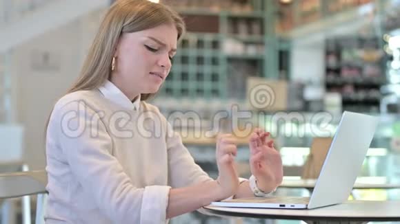 有手腕疼痛的年轻女子在咖啡馆用笔记本电脑视频的预览图