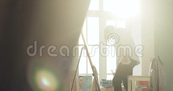 画师正在画一幅画在画架上站在窗户附近侧面看视频的预览图