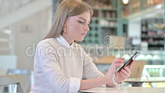 年轻女子在咖啡馆庆祝智能手机的成功视频的预览图