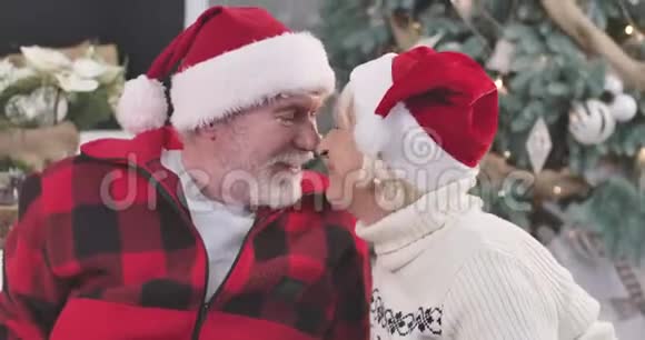 侧面看积极成熟的白种人夫妇脸微笑丈夫和妻子戴着圣诞帽摩擦鼻子接吻视频的预览图