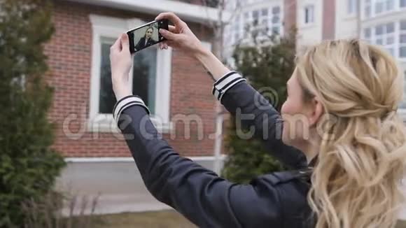 一个美丽的金发女孩的侧面肖像她用智能手机上网在一个郊区的家中拍摄自拍照片视频的预览图