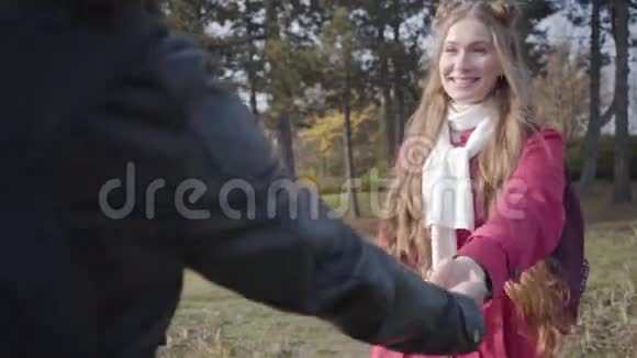 听我的想法微笑的金发女人牵着男人手走在秋天的公园里快乐的情侣在户外约会视频的预览图