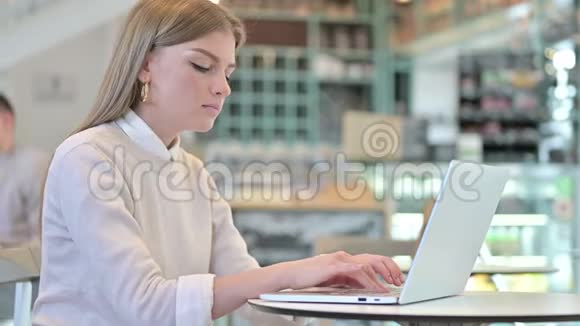 在咖啡馆里对着摄像机微笑的年轻女子使用笔记本电脑视频的预览图