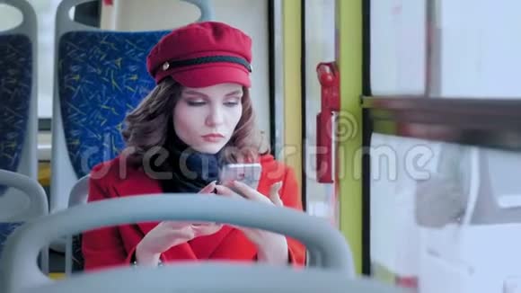 一个穿红色外套的优雅年轻女孩的肖像在公共交通中使用智能手机打印总线上的短信视频的预览图