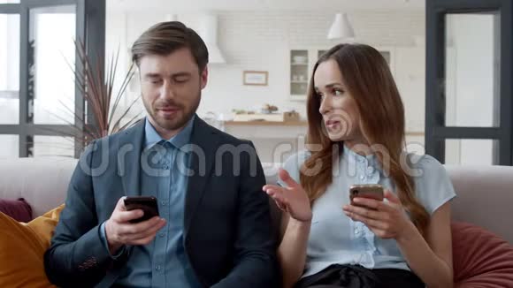 年轻女子在家里和丈夫说话两个人在手机上浏览互联网视频的预览图