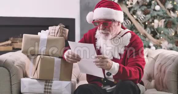 圣诞老人坐在礼物盒和读信的肖像戴着红色眼镜的老人在检查人们愿望视频的预览图