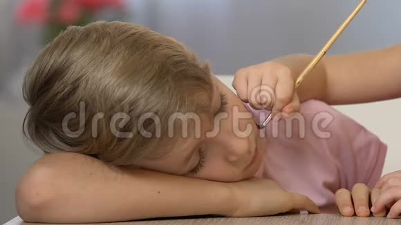 小妹妹在熟睡的男孩脸上画画快乐的童年滑稽的恶作剧视频的预览图