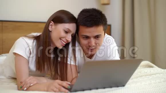 年轻快乐的白种人男人和女人躺在床上说话用笔记本电脑视频的预览图