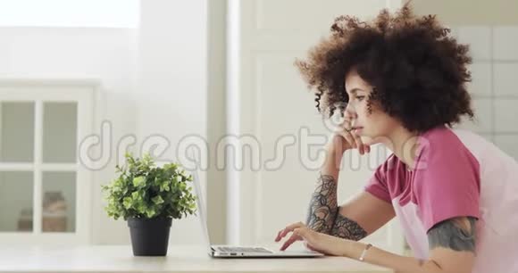 年轻的女性自由职业者卷发在家里的笔记本电脑上工作侧视视频的预览图