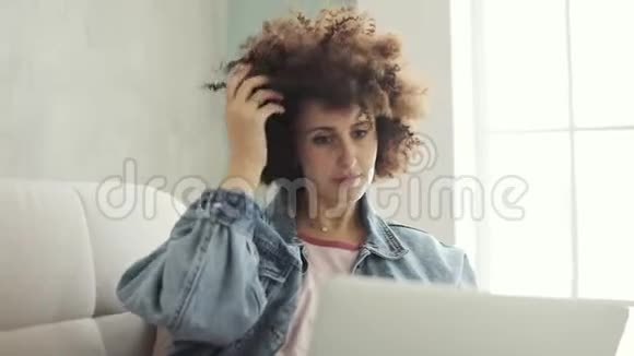 坐在沙发上的笔记本电脑上有卷发的女人在社交媒体上留言视频的预览图