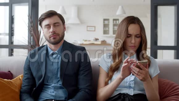 年轻夫妇坐在现代房间的沙发上疲倦的人睡沙发视频的预览图