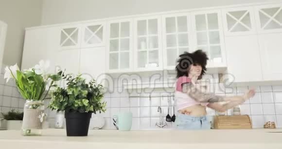 幸福的卷发年轻女子在家里的厨房里跳舞唱歌视频的预览图
