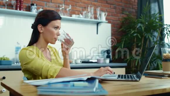 兴奋的女人在笔记本上读好消息女孩在厨房里喝水视频的预览图