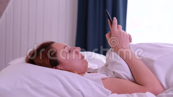 红头发的女人早上醒来开始使用她的智能手机视频的预览图