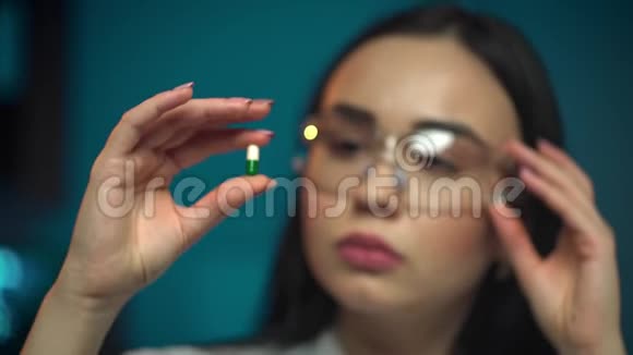 年轻漂亮的女科学家戴着防护眼镜手里拿着一颗透明药丸手套里戴着手指视频的预览图