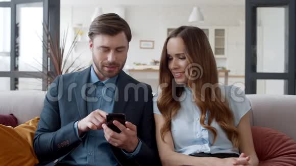 微笑的夫妇在家办公室看手机嘲笑男人和女人视频的预览图