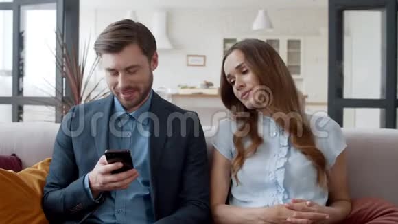 商务夫妇一起在沙发上放松惹眼的女人看着男人的电话视频的预览图