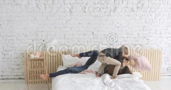 一家人的母亲和儿子在床上玩着有趣的枕头大战躺在床上拥抱在一起视频的预览图