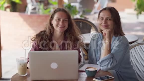 快乐的女性朋友在户外咖啡馆和笔记本电脑一起工作的画像视频的预览图
