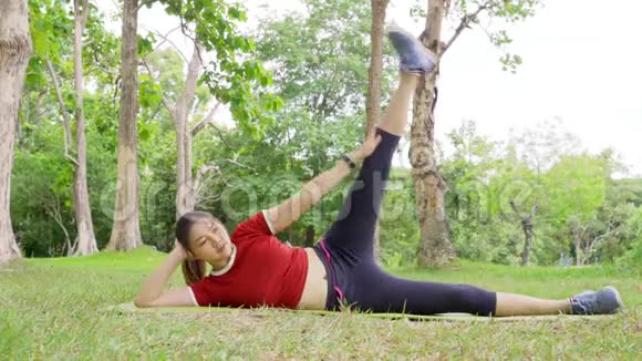 年轻健康快乐的亚洲女人一边躺着一边在当地一个公园晨练一边做着她的举重运动视频的预览图