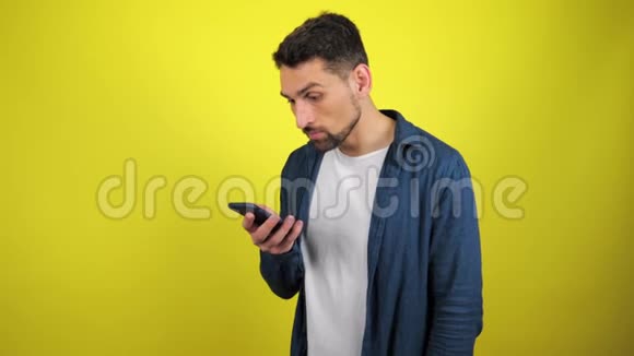 一个穿着蓝色衬衫和白色T恤的年轻人看着相机拿着智能手机惊讶地说哇视频的预览图