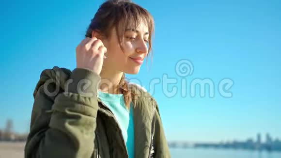 年轻漂亮的女士在户外使用无线耳机做双人水龙头视频的预览图