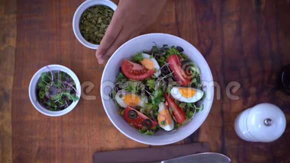女人用生菜番茄鸡蛋和橄榄做的新鲜沙拉南瓜子豆芽和盐胡椒视频的预览图
