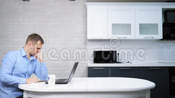 商人坐在厨房的桌子旁用他的笔记本电脑视频的预览图