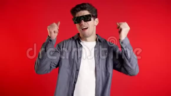英俊的男人带着发光的迪斯科眼镜在红色的背景上跳舞视频的预览图