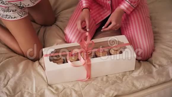女孩们拿着礼物坐在床上用美味的纸杯蛋糕打开盒子视频的预览图