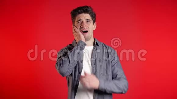 穿牛仔衬衫的年轻人红色工作室背景上有牙齿疼痛牙痛视频的预览图