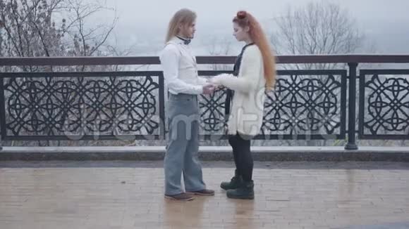 侧面观察年轻的白种人男子抓住他的女朋友手和交谈快乐的一对夫妇面对面地站在秋天视频的预览图