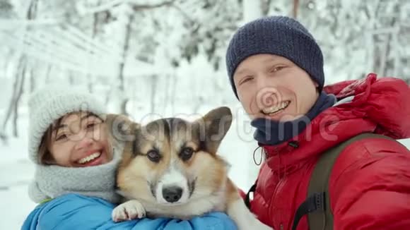 快乐的微笑年轻夫妇自拍与威尔士科尔吉狗在雪冬公园在寒冷的冬天视频的预览图