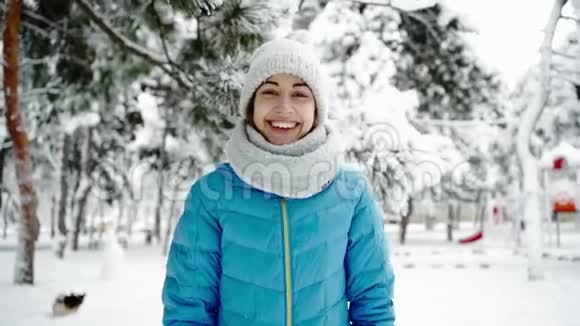 慢镜头特写美丽微笑的年轻女子穿着温暖的羊毛帽戴着长长的围巾在下雪的冬天散步视频的预览图
