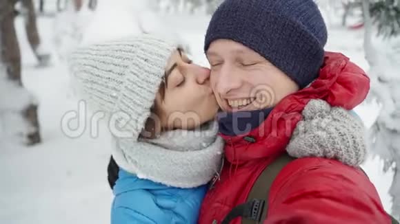 在寒冷的冬天一对幸福的微笑的年轻夫妇在白雪皑皑的冬季公园散步的特写肖像男人和女人很可爱视频的预览图