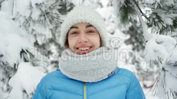 可爱的微笑的年轻女子戴着温暖的羊毛帽和长长的围巾在白雪皑皑的冬季公园里散步视频的预览图