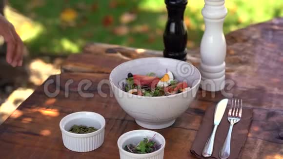 女人的手调味着一种新鲜的沙拉由生菜番茄鸡蛋和橄榄制成南瓜子豆芽和盐胡椒视频的预览图