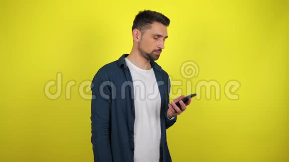 一个穿着蓝色衬衫和白色T恤的年轻人在智能手机上打电话微笑着视频的预览图