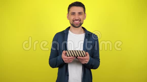 一个身穿白色T恤的男人手里拿着一个盒子手里拿着一件礼物微笑着看着相机视频的预览图