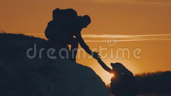 在两个登山者之间帮忙的剪影两个徒步旅行者在山顶上一个男人帮助一个女人攀登一个纯粹的视频的预览图