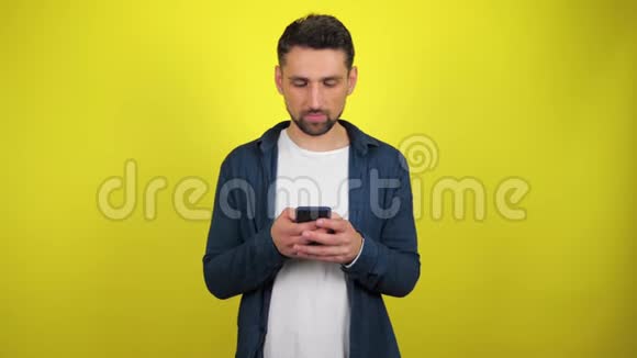一个穿着蓝色衬衫和白色T恤的年轻人饶有兴趣地微笑着使用智能手机视频的预览图