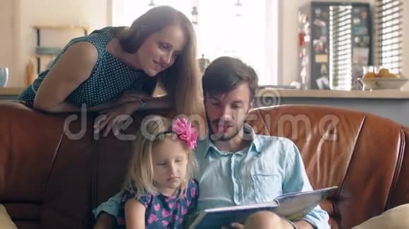 家庭幸福年轻的父亲和他的金发小女儿正在餐厅的皮革沙发上读一个故事4K视频的预览图